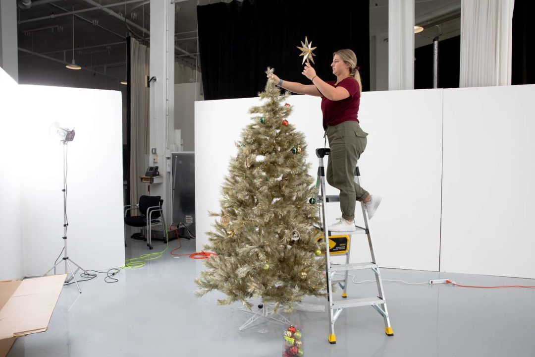 A lady standing up on a ladder decorating a Christmas tree.
